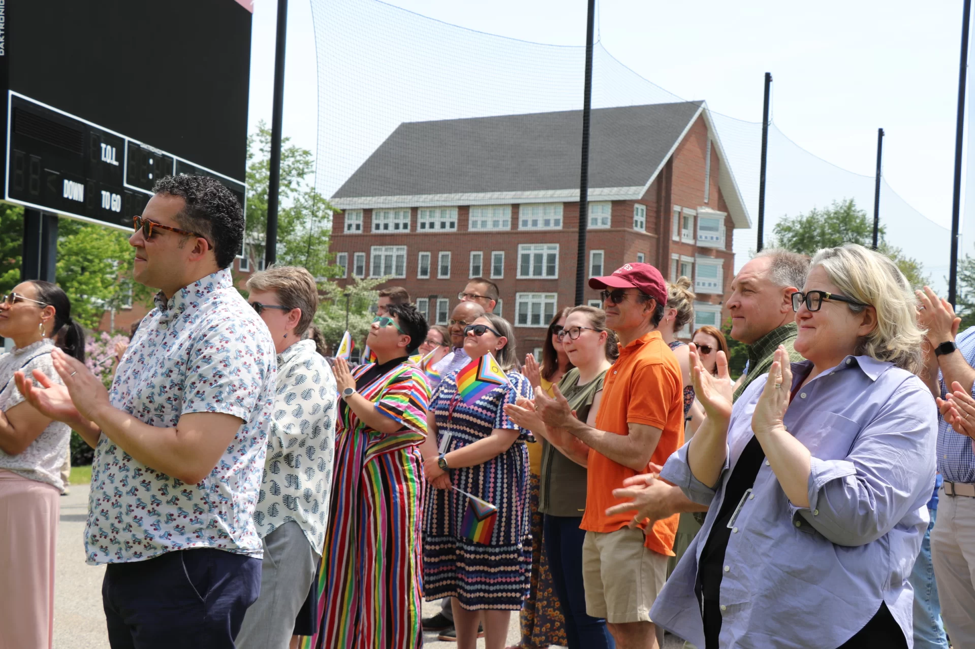 A group of people cheer and clap, waving Pride flags