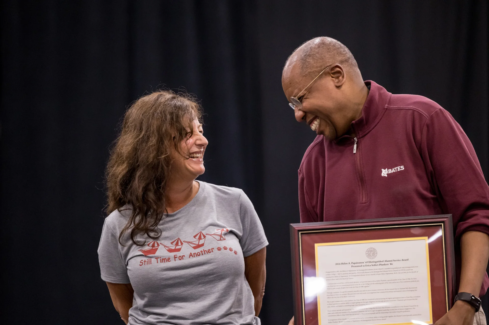 Two people smiling on a stage while one holds an award