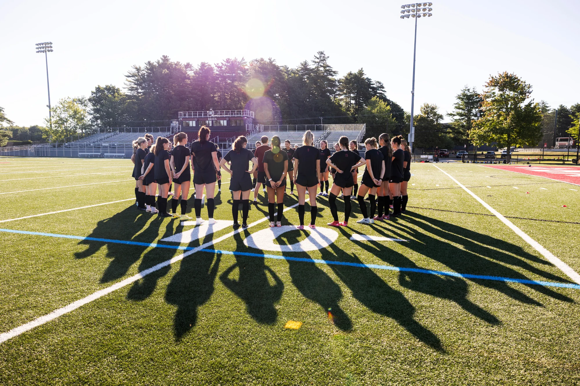 A group of soccer players huddle on a sunny field