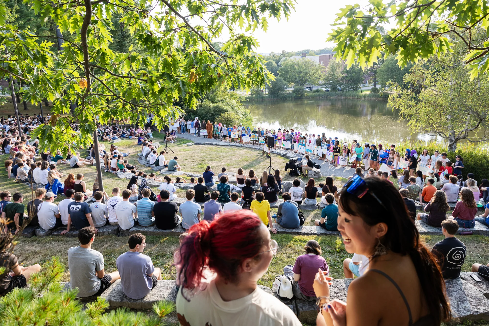 A group of students in colorful clothing gather in an an outdoor amphitheater on a sunny day