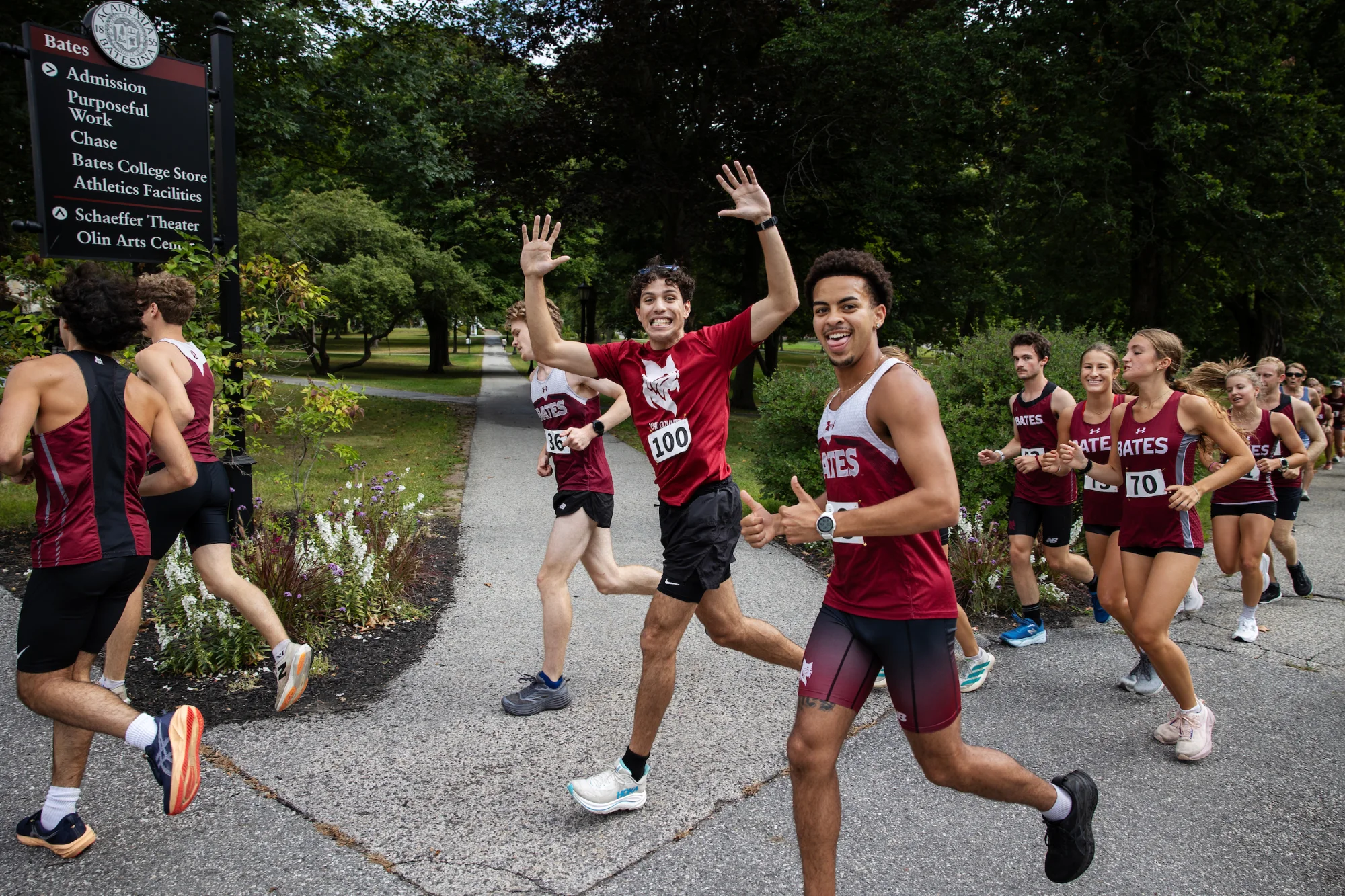 More than a dozen runners in uniform run by, with two at the center smiling into the camera