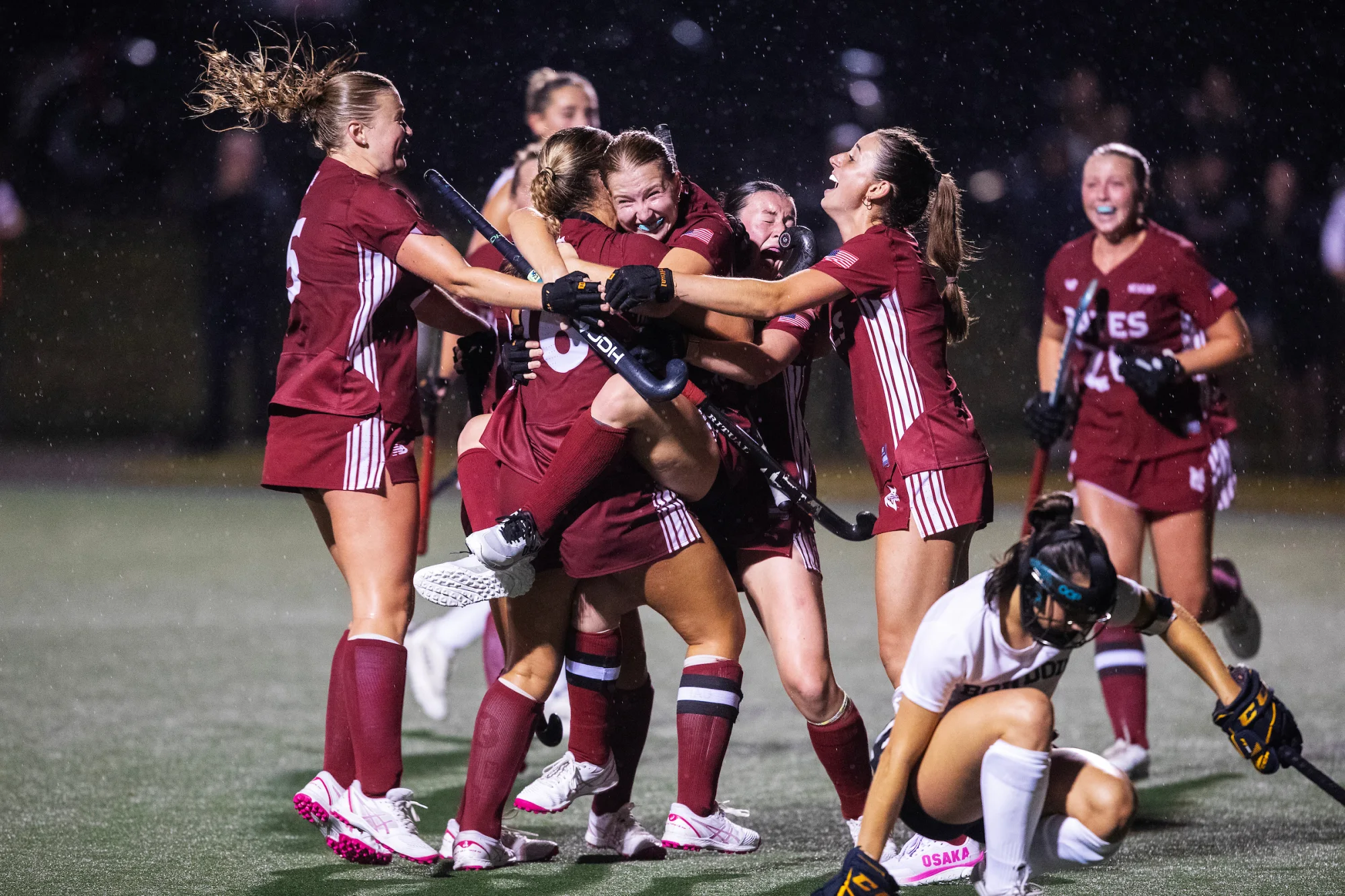 Field hockeys players cheer and embrace, one jumping into another's arms