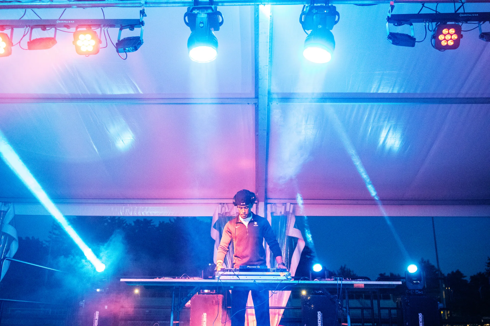 A person stands on a stage with headphones on, DJing