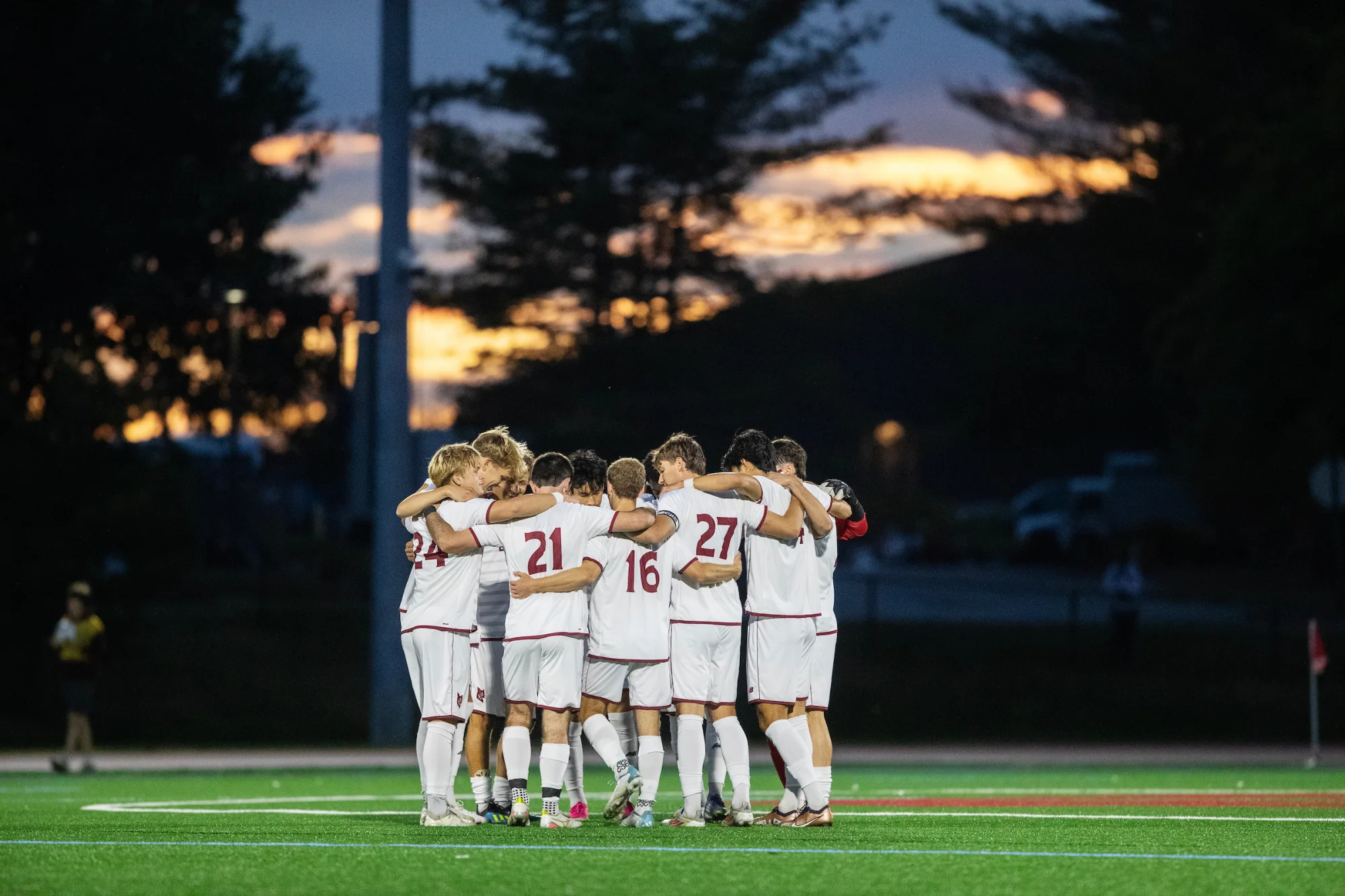 A group of soccer players huddles beneath a sunset