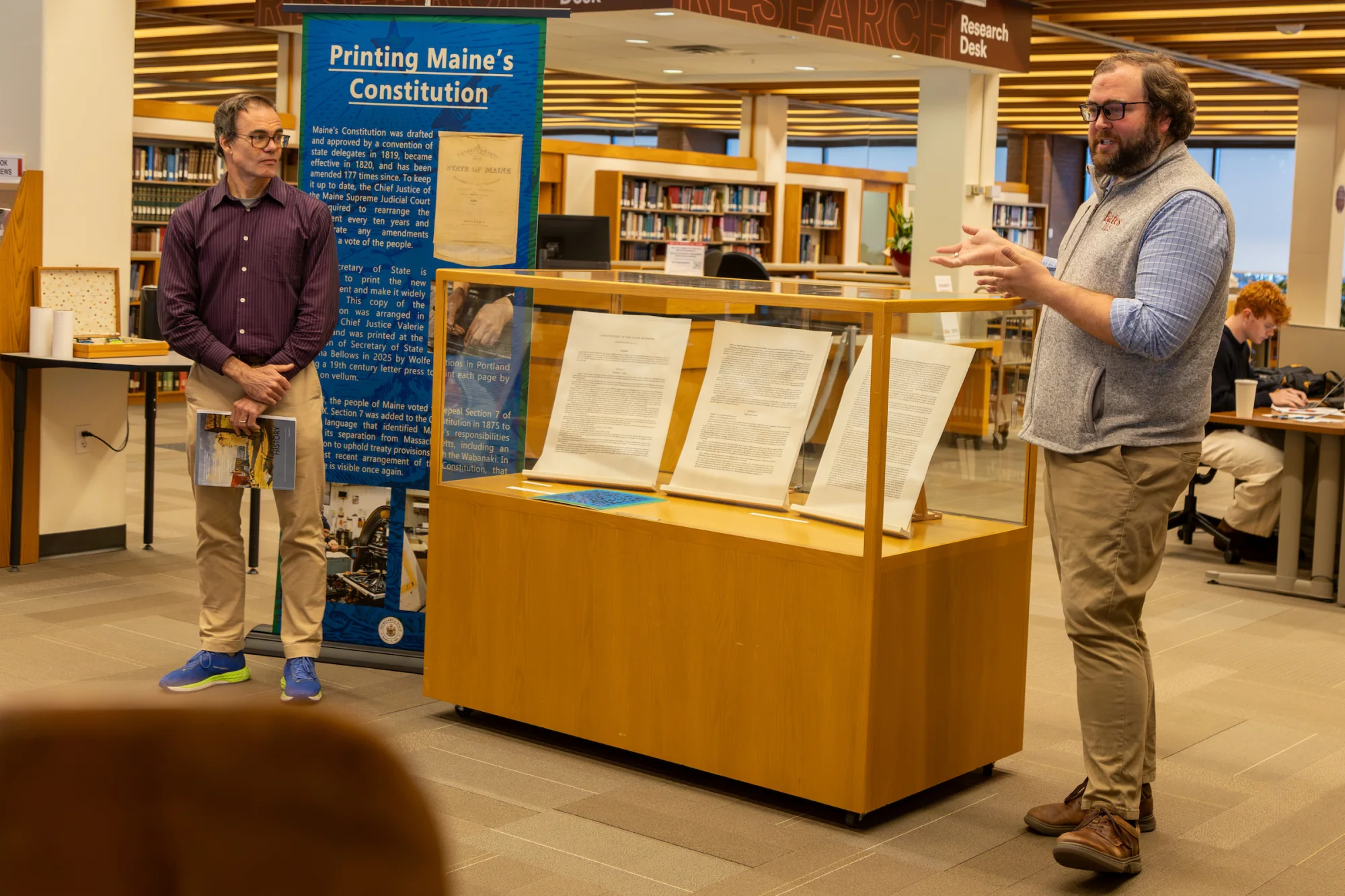 Associate Professor of History Joe Hall and Sam Howes, the TK flank the display of the 2026 printing of the Maine State Constitution, which features restored sections of the document that had been redacted in 1876. Photo by Carly Philpott '27 for Bates College