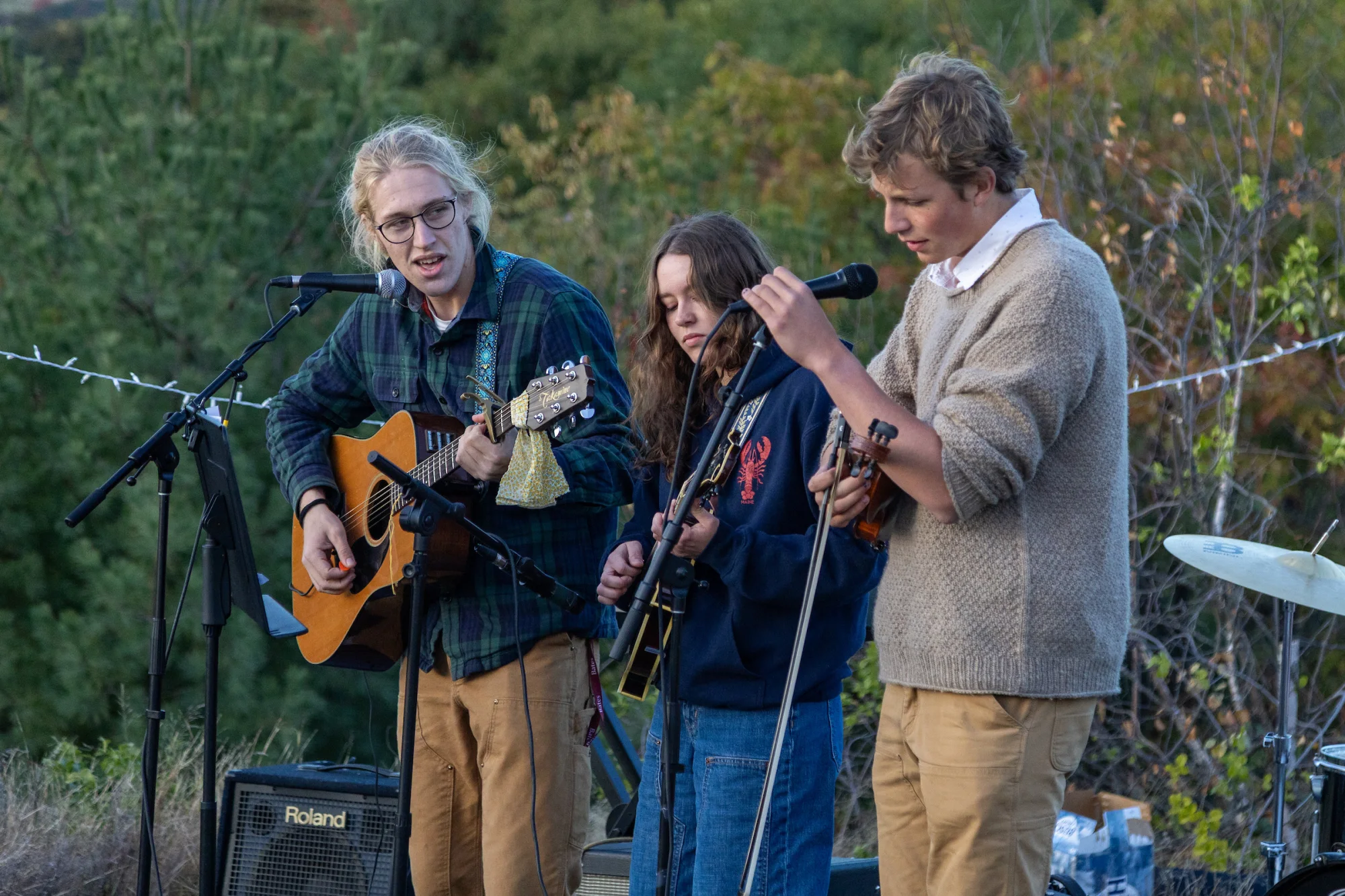 Three people perform outside, with two of them playing instruments