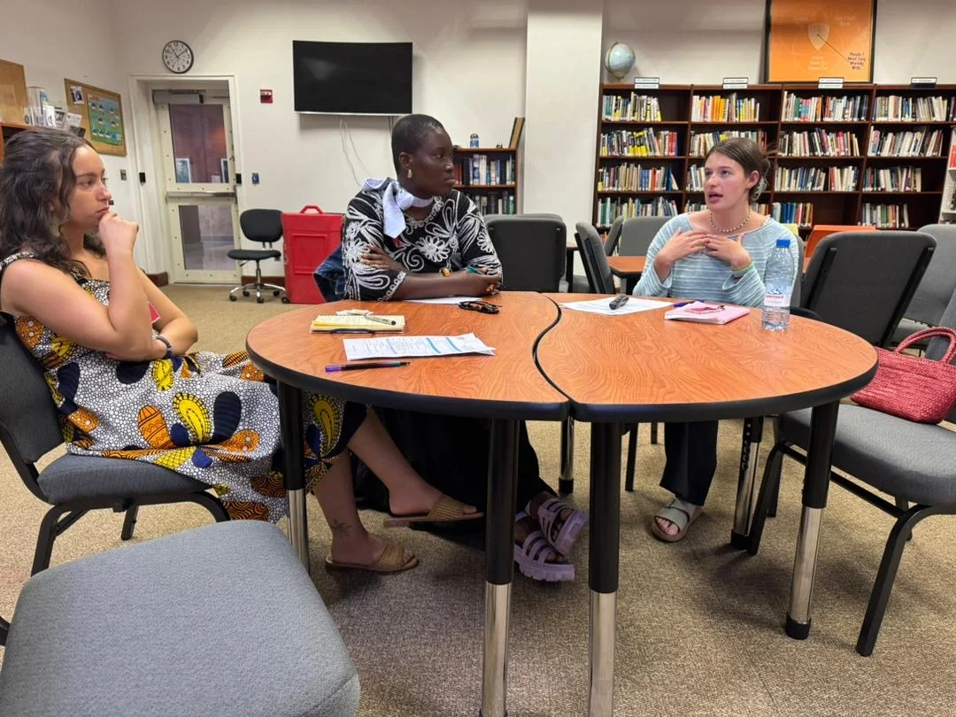 Three women sit around a table in a room lined with shelves of books