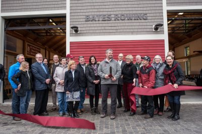 Flanked by Bates rowing supporters and college leaders, head coach Peter Steenstra cuts the ribbon during the dedication of the rowing boathouse on Oct. 29. (Andree Kehn for Bates College)