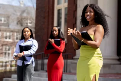 “After four years of working towards our majors together, spending late nights in Bonney covering boards full of equations, what was hard work is now a small picture of who we are, and a snippet of what college was to us. I want to thank you guys for doing it with me and for being a part of me.”

— Blessing Akinmade ’25, a biochemistry major from Newark, N.J., addressing Sophia Ibeh ’25 and Darlene Igiraneza ‘25.

Billed as “Sophia + Darlene + Blessing’s Thesis Binding,” the gathering personified the Bates ritual of thesis binding with three seniors who acknowledged friends, family, faculty, and staff who supported and loved them along the way.

Akinmade’s thesis, “Translation: Borrelia Burgdorferi, The Causative Agent in Lyme Disease,” was written under the supervision of Stella James Sims Professor of Chemistry and Biochemistry Paula Schlax.

Ibeh, a biochemistry major with a concentration in the human body, from Houston, wrote her thesis, “Enzymes, Equity, and Expression: The Role of Cytochrome P450 Genetic Variability in Drug Metabolism and Racial Disparities in Clinical Outcomes for Black Patients,” under the supervision of Assistant Professor of Chemistry and Biochemistry Dylan Freas.

Igiraneza, a biology major from Glendale, Ariz., wrote her thesis, “Barriers of Survival: A Literature Review on Neonatal Mortality and Health Disparities,” under the supervision of Wagener Family Professor of Equity and Inclusion in STEM April Horton.

After speaking and binding, the three seniors toasted the moment with an uncorked spray of champagne on the steps of Coram Library midday on Friday, April 18.