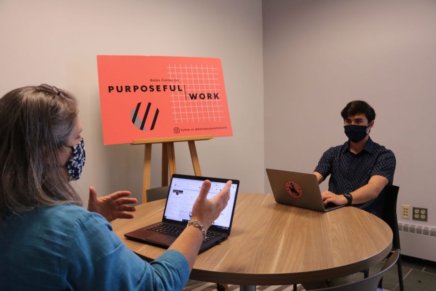 A student and an advisor sit across a round table from each other, both using laptops and wearing face masks