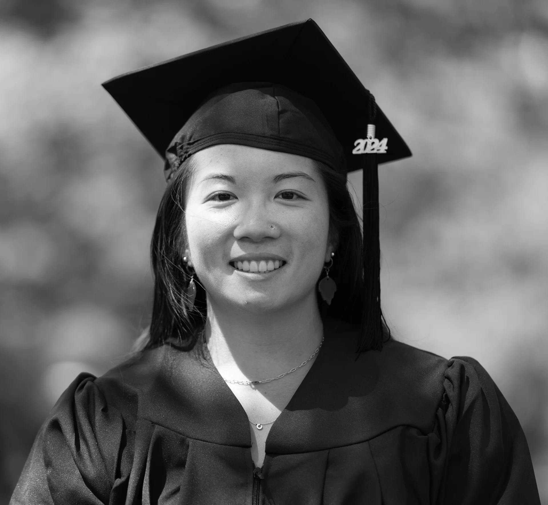 Black and white photo of Caitlin standing outdoors wearing her cap and gown